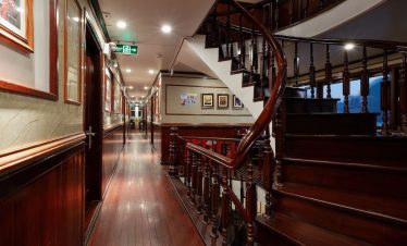 Elegant cruise interior with wooden staircase and classic decor in Halong Bay.