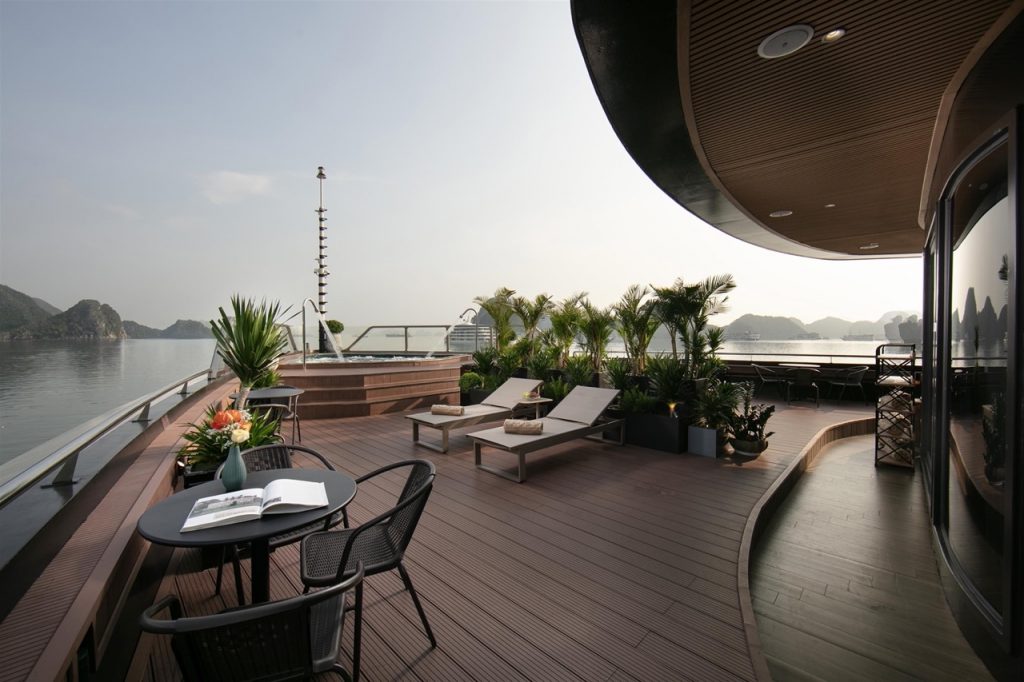 Stunning cruise balcony overlooking Halong Bay with comfortable lounge chairs and lush plants, perfe.