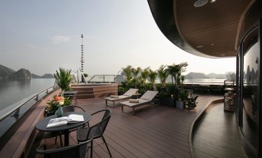 Stunning cruise balcony overlooking Halong Bay with comfortable lounge chairs and lush plants, perfe.