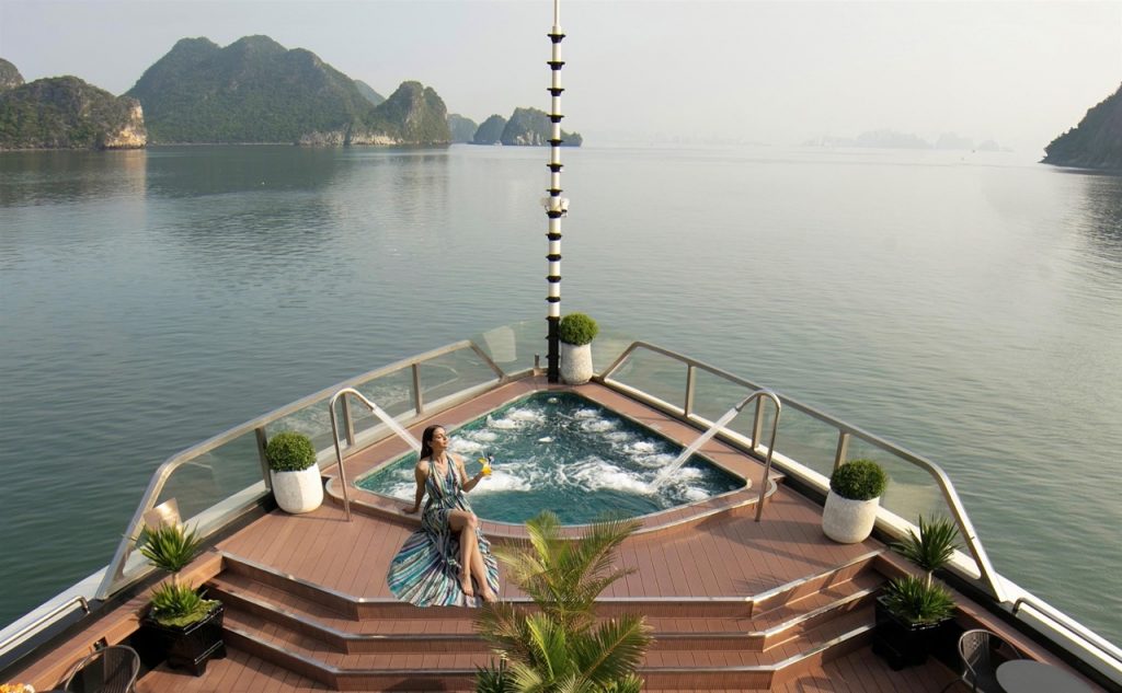 Relaxing woman enjoying hot tub on Halong Bay cruise balcony with scenic limestone islands.