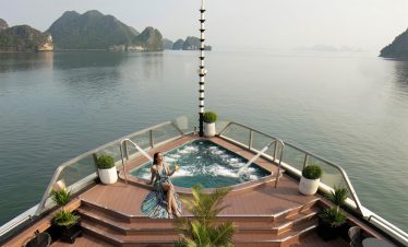 Relaxing woman enjoying hot tub on Halong Bay cruise balcony with scenic limestone islands.