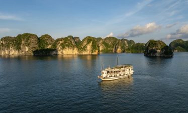 A cruise boat sailing through the stunning limestone karsts of Halong Bay under clear blue skies.
