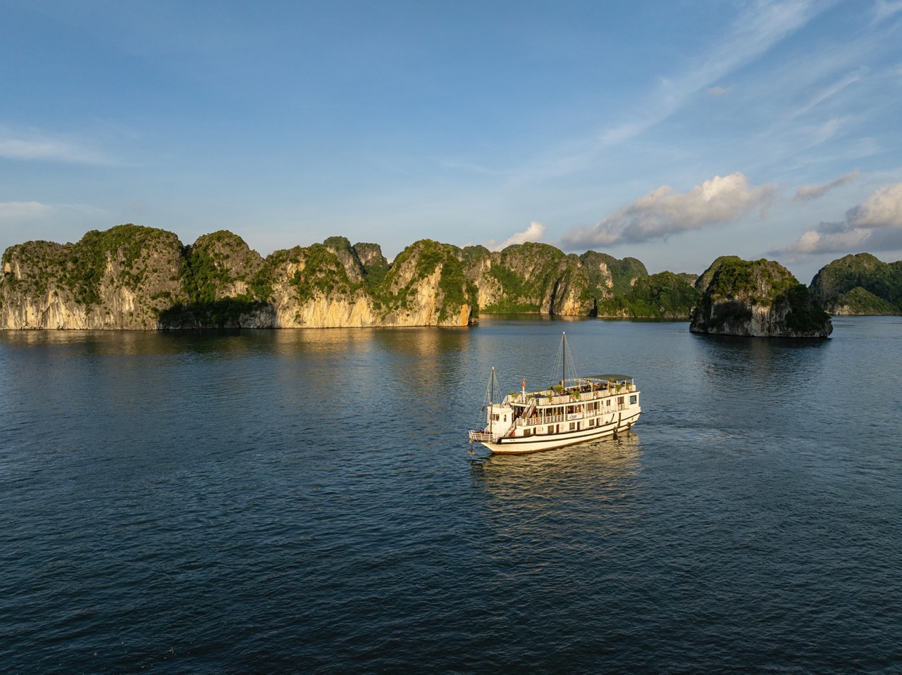 A cruise boat sailing through the stunning limestone karsts of Halong Bay under clear blue skies.