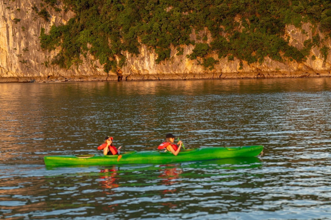 Kayaking adventure on Halong Bay cruise balcony with scenic limestone cliffs.