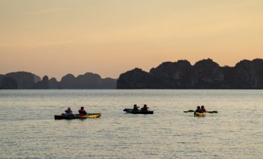 Kayaking on Halong Bay at sunset with scenic limestone islands in the background.