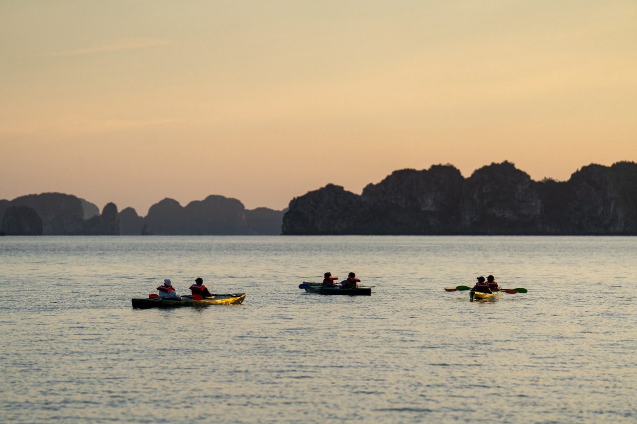 Kayaking on Halong Bay at sunset with scenic limestone islands in the background.