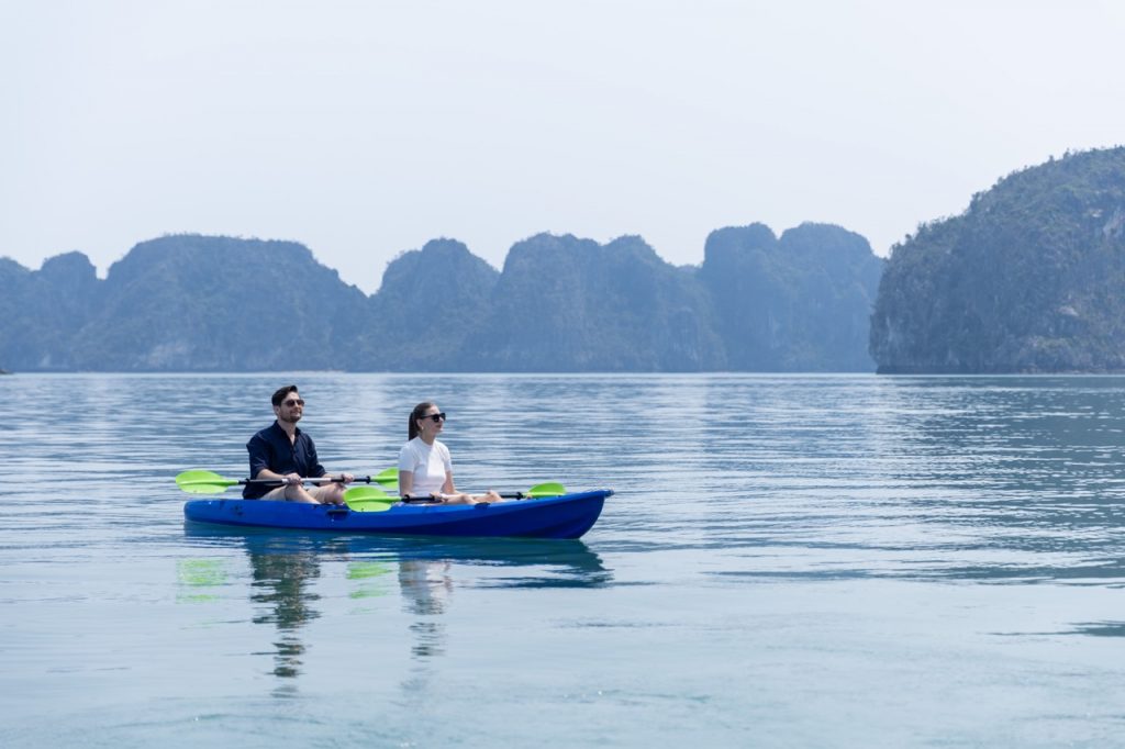 People kayaking on calm Halong Bay waters with limestone islands in the background.