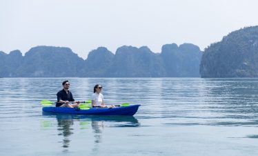 People kayaking on calm Halong Bay waters with limestone islands in the background.