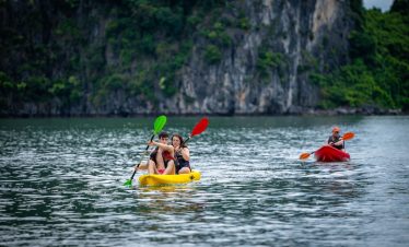 Kayakers paddling on calm Halong Bay waters with lush green cliffs in the background, enjoying a pea.