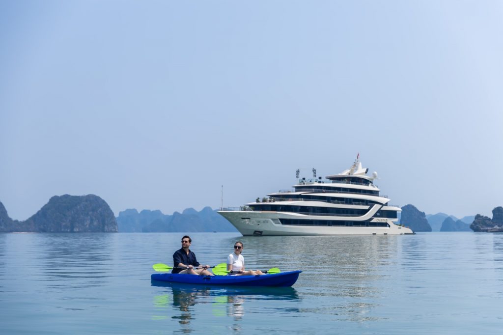 People kayaking on calm Halong Bay waters with scenic limestone islands in the background.
