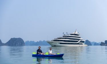 People kayaking on calm Halong Bay waters with scenic limestone islands in the background.