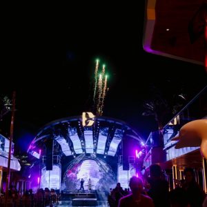 Firework display at night during a live outdoor music event with colorful stage lighting.