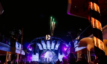 Firework display at night during a live outdoor music event with colorful stage lighting.