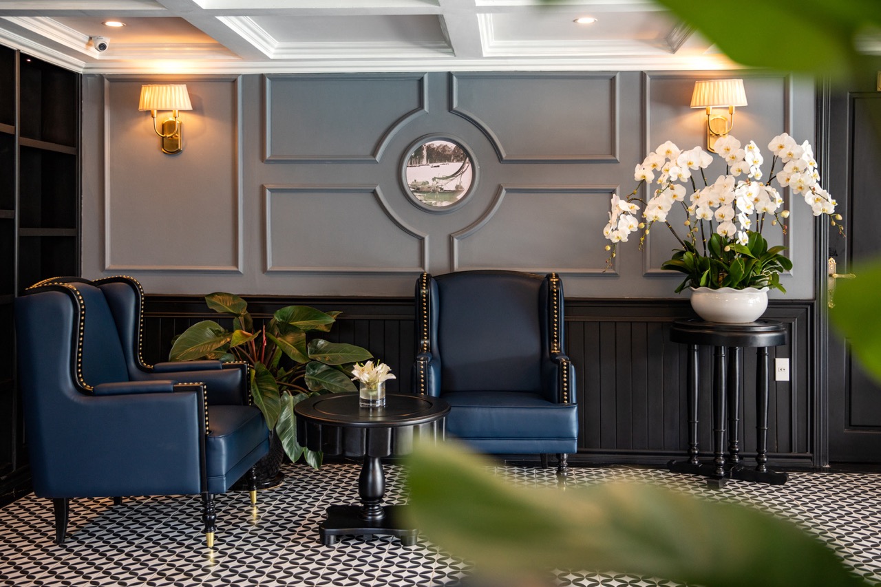 Elegant cruise lounge with navy blue armchairs and floral decor in Halong Bay. Perfect for relaxing.