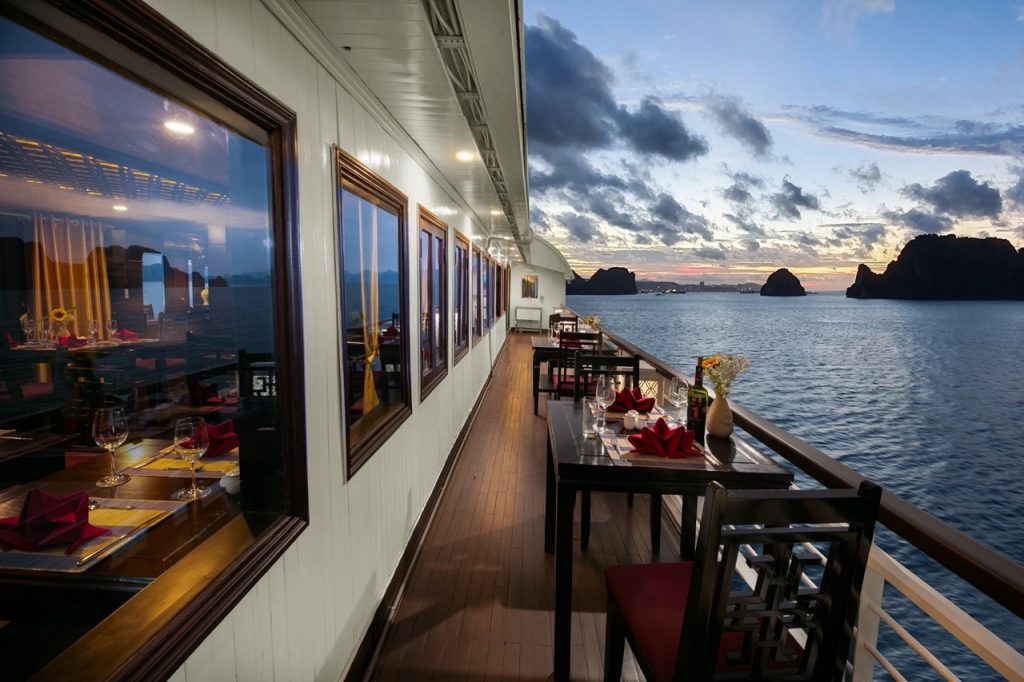 Stunning sunset view from the cruise balcony over Halong Bay, with calm waters and dramatic limeston.