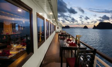 Stunning sunset view from the cruise balcony over Halong Bay, with calm waters and dramatic limeston.