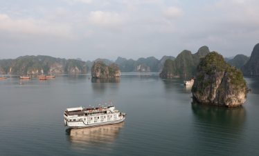 Scenic view of a cruise sailing among limestone karsts in Halong Bay, Vietnam, with calm waters and.
