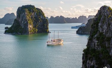 Scenic view of limestone islands and emerald waters in Bai Tu Long Bay with a traditional cruise boa.