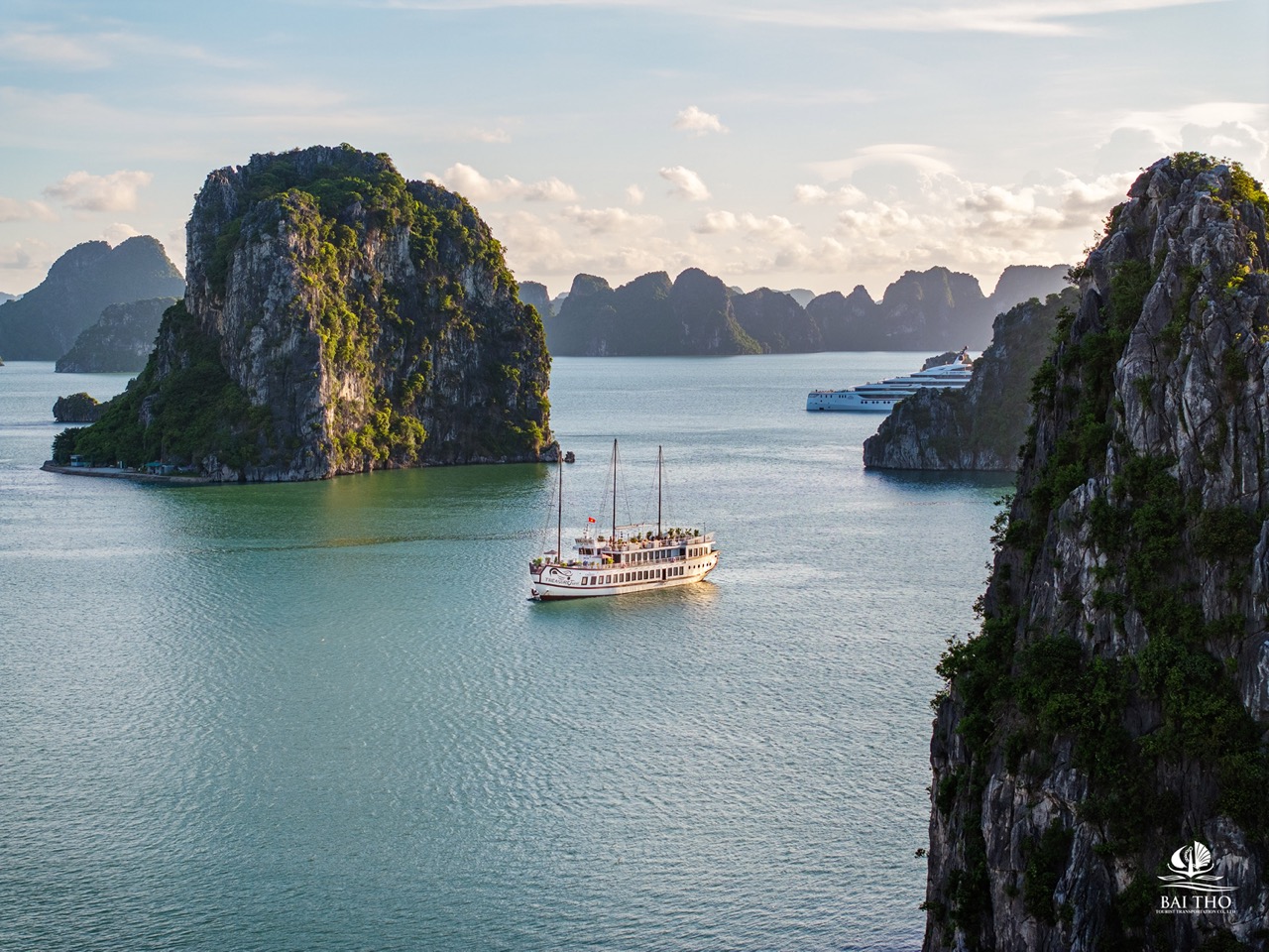 Scenic view of limestone islands and emerald waters in Bai Tu Long Bay with a traditional cruise boa.