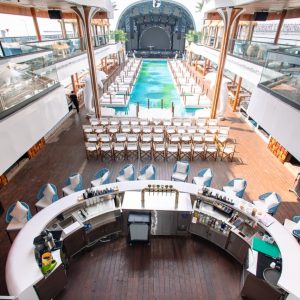 Luxury cruise ship deck with swimming pool, bar, and panoramic views.