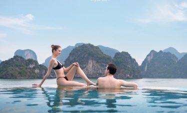 Relaxing couple on cruise balcony with stunning Halong Bay scenery, clear blue sky and limestone kar.