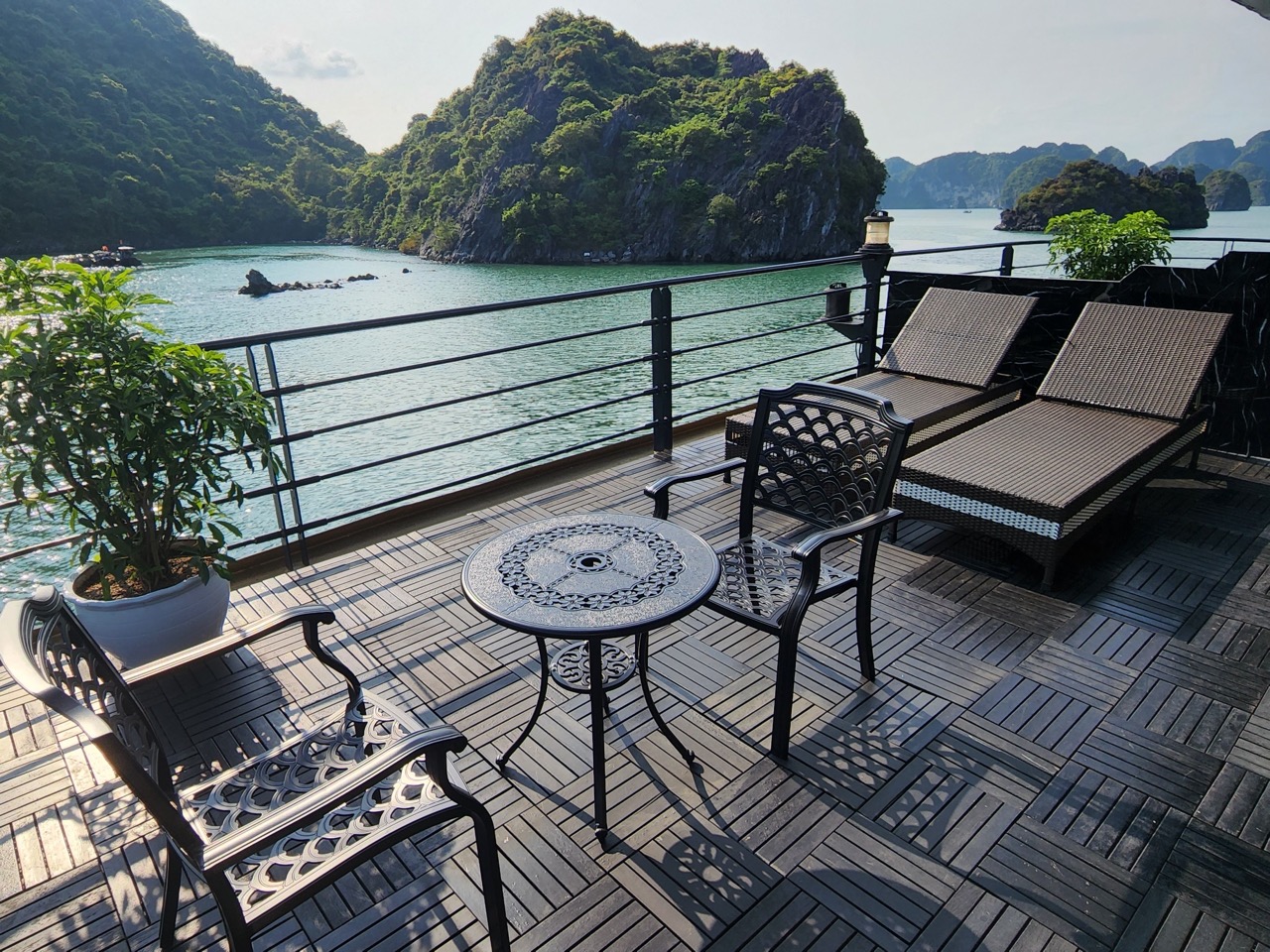 Scenic view of Halong Bay from a cruise balcony with relaxing chairs and lush islands in the backgro.