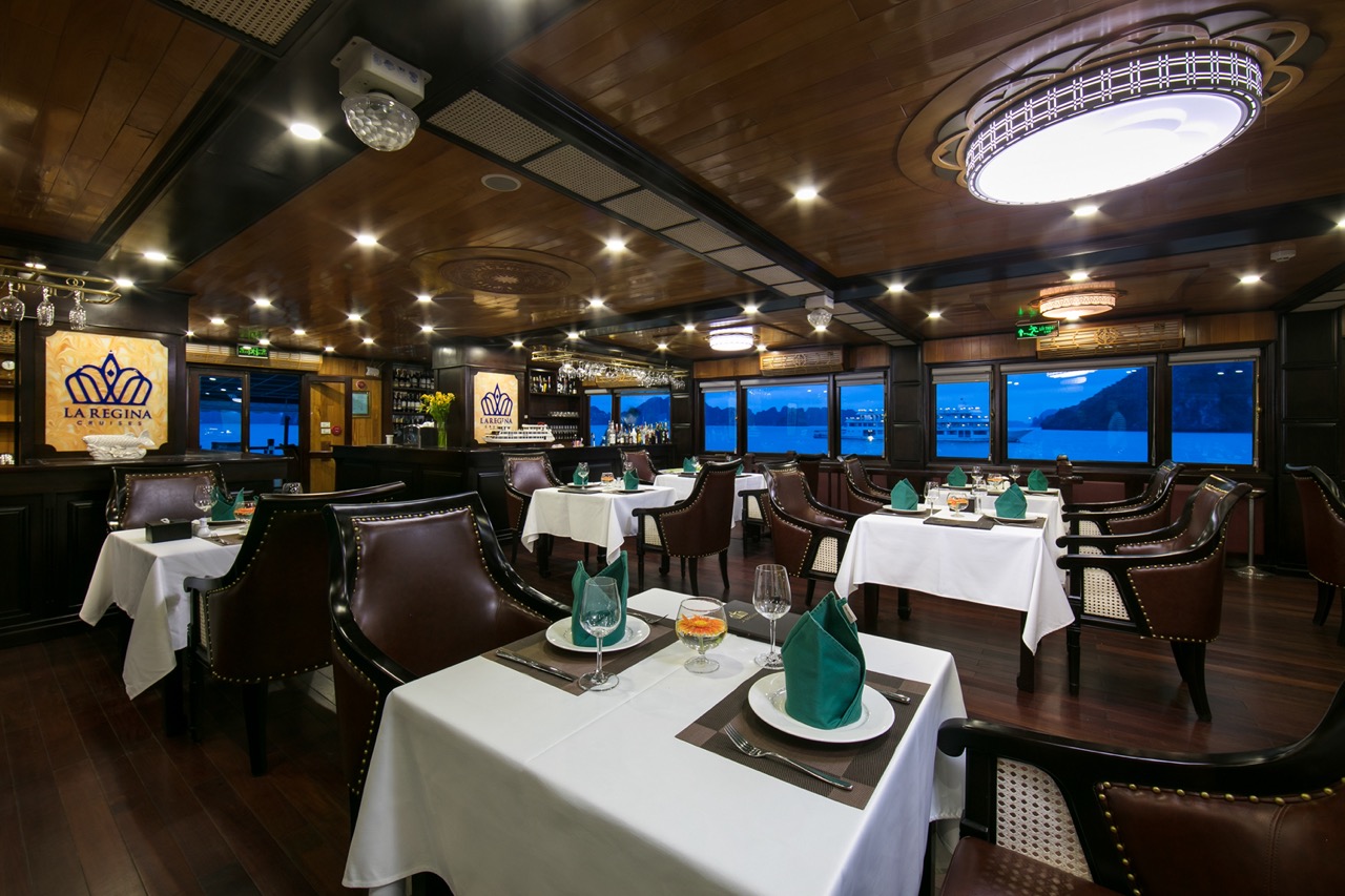 Stunning Halong Bay cruise interior with panoramic views, elegant table settings, and cozy ambiance.
