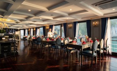 Elegant cruise dining room overlooking Halong Bay with luxurious decor and large windows.