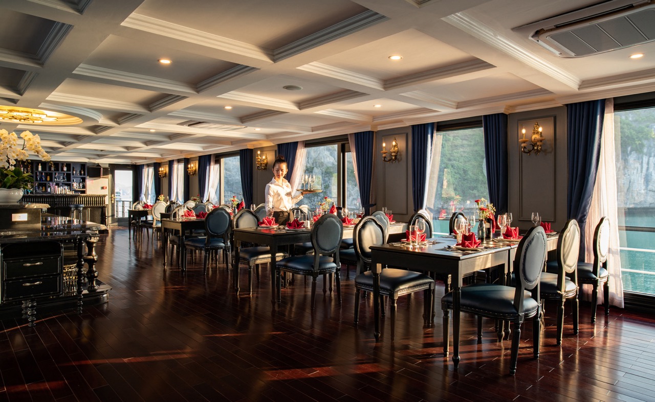 Elegant cruise dining room overlooking Halong Bay with luxurious decor and large windows.