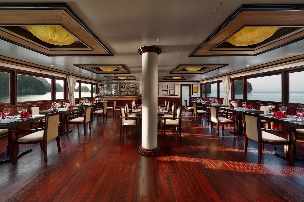 Spacious cruise dining room with large windows overlooking Halong Bay, elegant wooden decor, perfect.