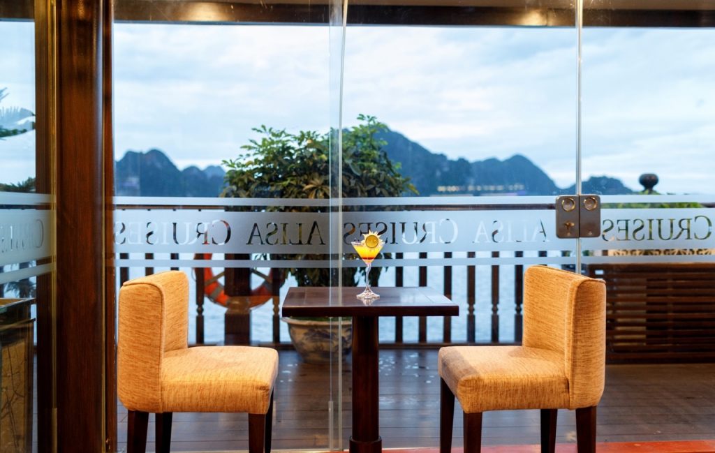 Scenic view of Halong Bay from a cruise balcony with two chairs and a table, perfect for relaxing an.