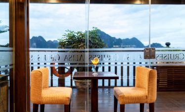 Scenic view of Halong Bay from a cruise balcony with two chairs and a table, perfect for relaxing an.