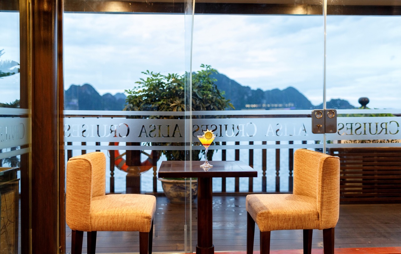 Scenic view of Halong Bay from a cruise balcony with two chairs and a table, perfect for relaxing an.