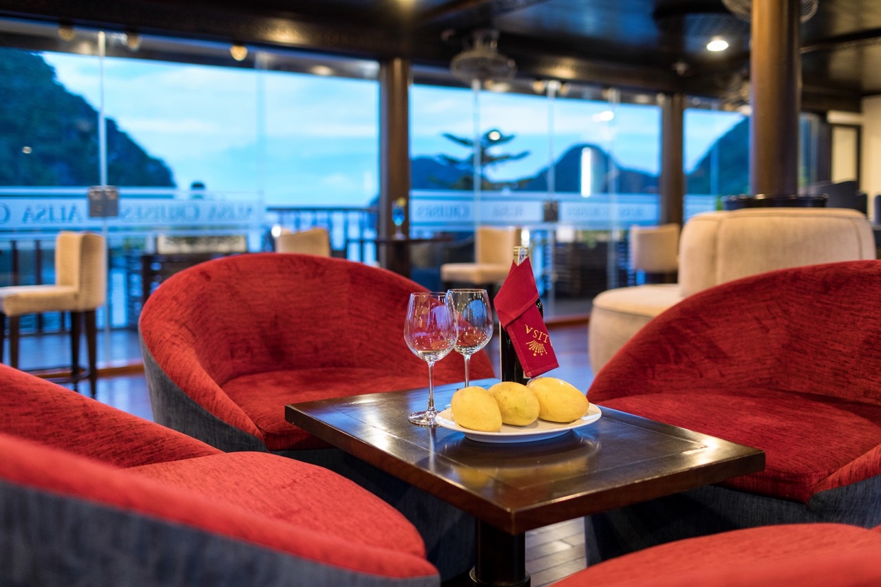 Scenic view of Halong Bay from a cruise balcony with cozy seating and sunset ambiance.