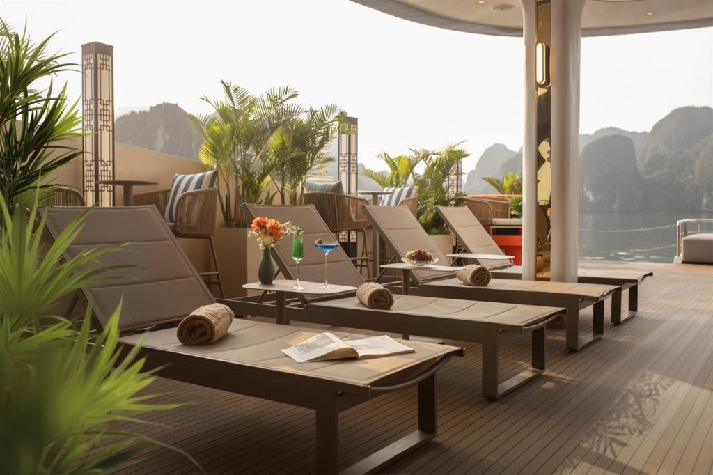 Scenic Halong Bay cruise balcony with lounge chairs and lush greenery, perfect for relaxing and enjo.