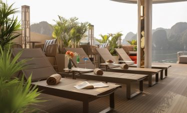 Scenic Halong Bay cruise balcony with lounge chairs and lush greenery, perfect for relaxing and enjo.