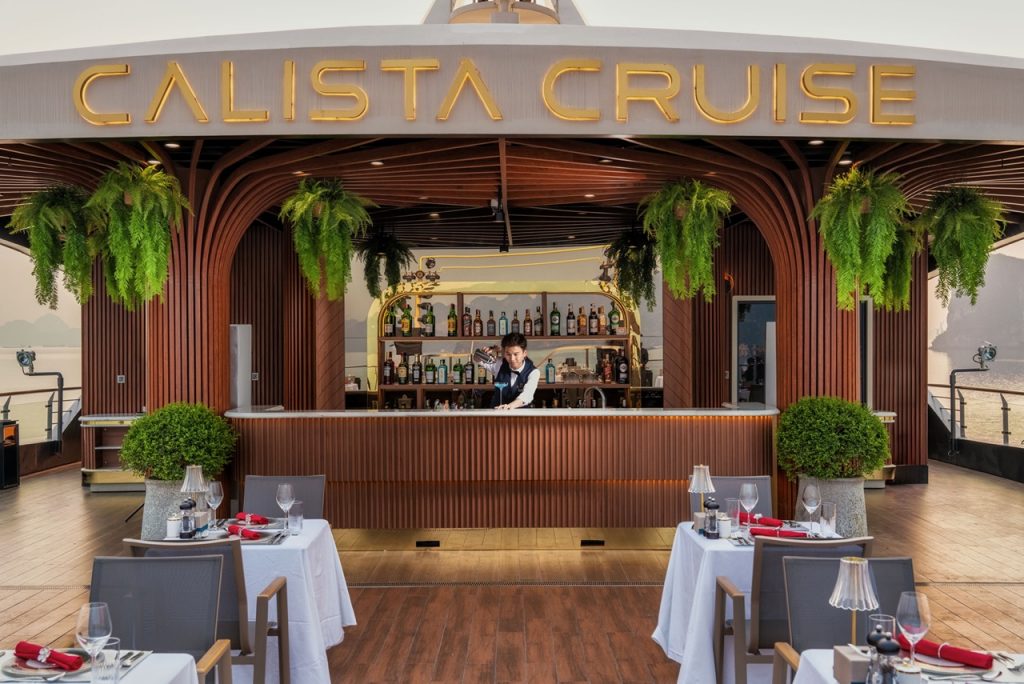 Elegant cruise balcony scene with dining setup and lush greenery in Halong Bay.