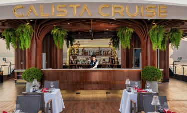 Elegant cruise balcony scene with dining setup and lush greenery in Halong Bay.