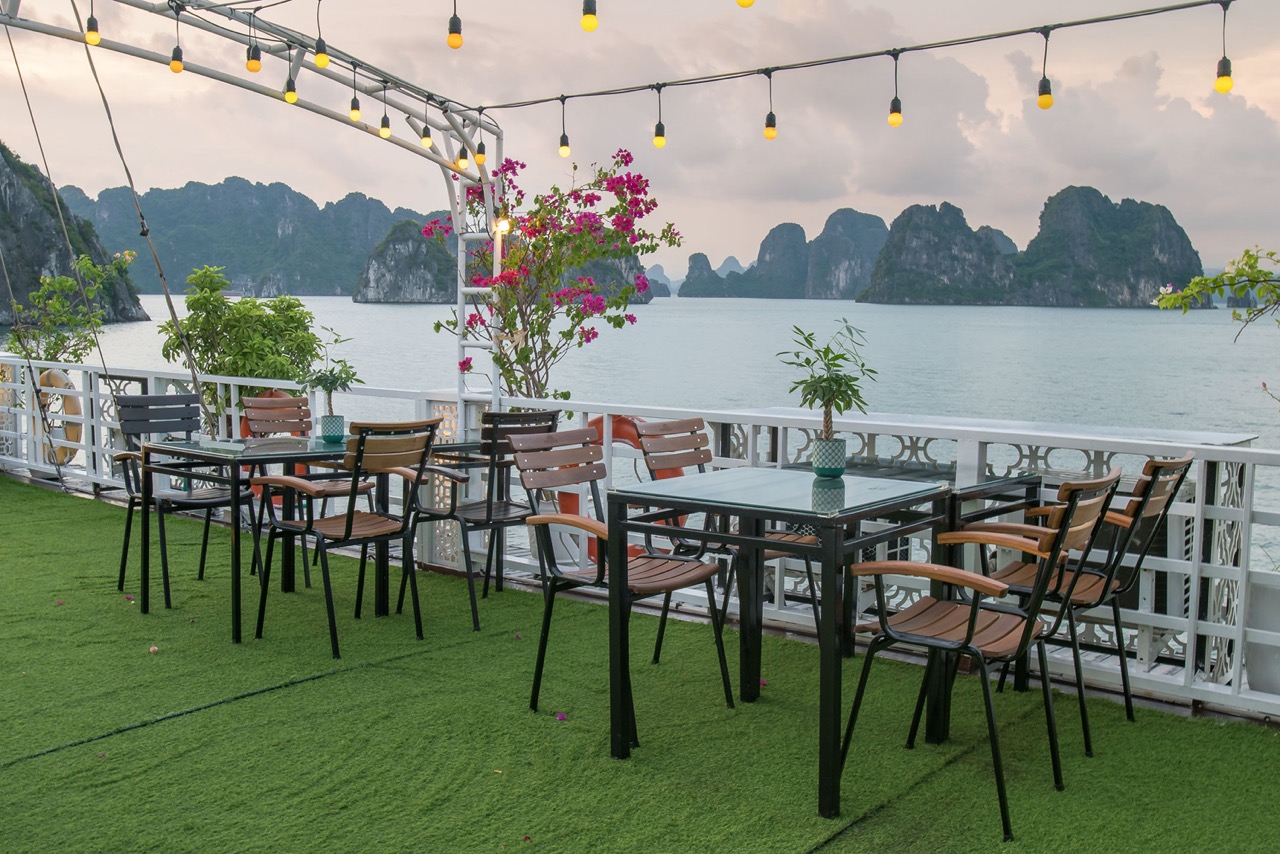 Stunning cruise balcony overlooking Halong Bay with seating, vibrant flowers, and scenic limestone i.