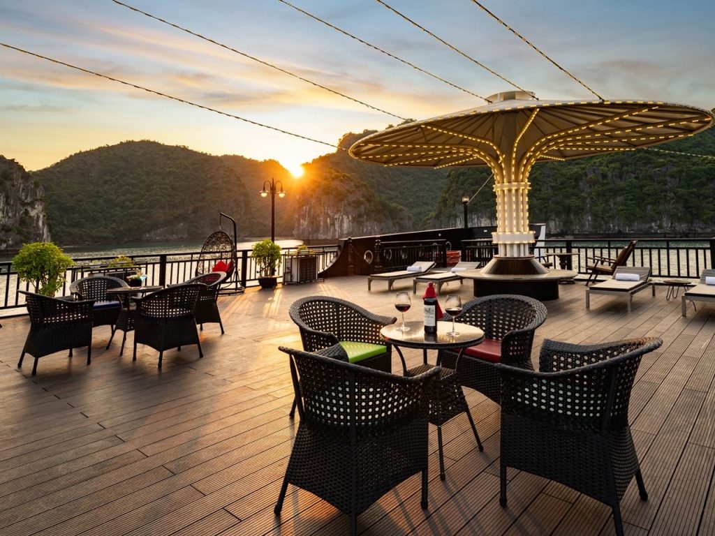 Stunning sunset view from cruise balcony in Halong Bay with scenic mountains and calm waters.