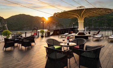 Stunning sunset view from cruise balcony in Halong Bay with scenic mountains and calm waters.