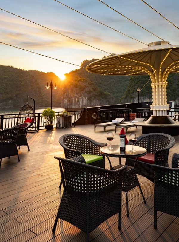 Stunning sunset view from cruise balcony in Halong Bay with scenic mountains and calm waters.
