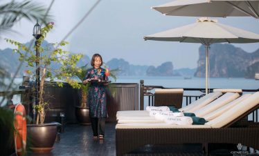 Scenic view of a woman enjoying a drink on a cruise balcony with loungers and umbrellas in Halong Ba.