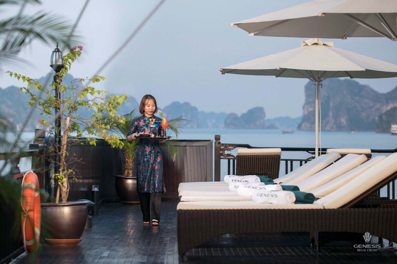 Scenic view of a woman enjoying a drink on a cruise balcony with loungers and umbrellas in Halong Ba.