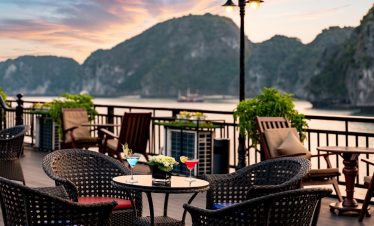 Stunning sunset over Halong Bay with a cruise balcony, featuring outdoor seating and scenic mountain.