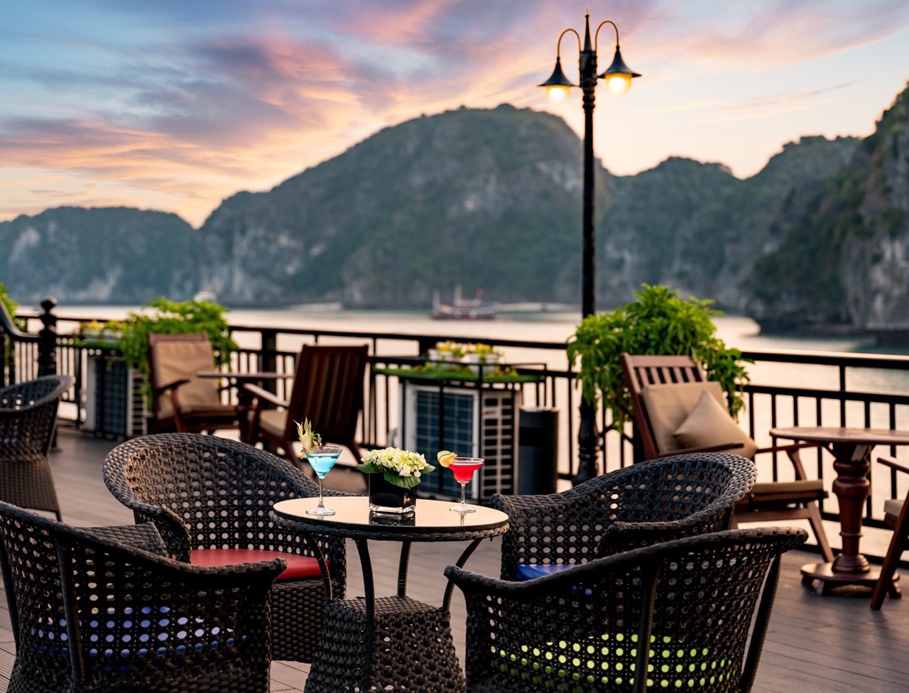 Stunning sunset over Halong Bay with a cruise balcony, featuring outdoor seating and scenic mountain.