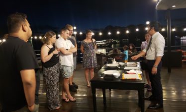 Halong Bay cruise dinner scene with guests enjoying a meal on the deck at night, scenic water views,.