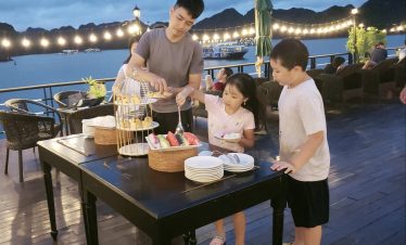Enjoying sunset on a Halong Bay cruise balcony with family and scenic mountain views.