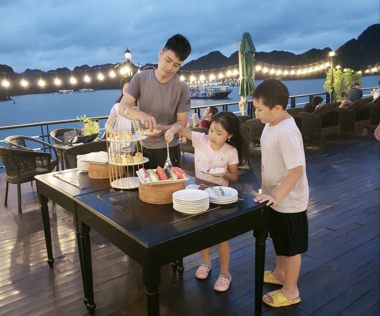 Enjoying sunset on a Halong Bay cruise balcony with family and scenic mountain views.