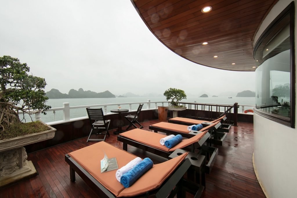 Scenic view of Halong Bay from a luxury cruise balcony with lounge chairs and relaxing atmosphere.